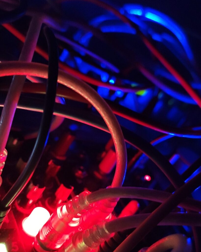 Dettaglio di sintetizzatore modulare con cavi patch e luci LED colorate.